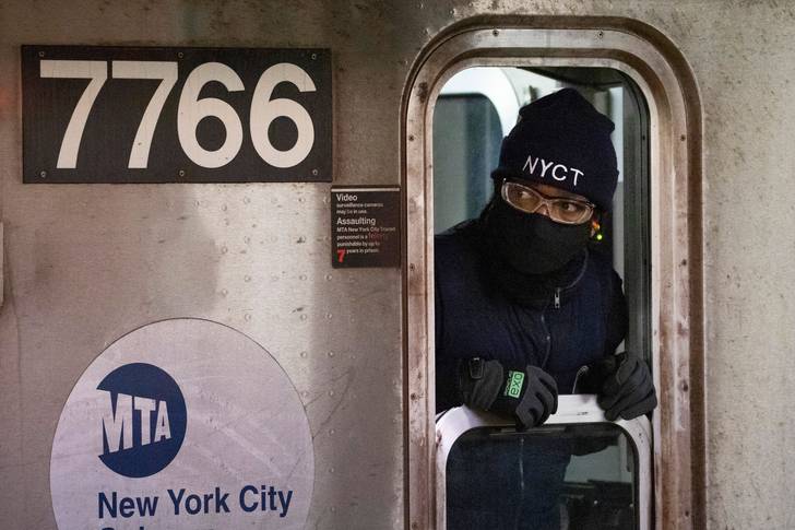 Subway conductor wearing a fa e mask looks out a window to check on passengers entering and leaving the train, in the Bronx borough of New York
